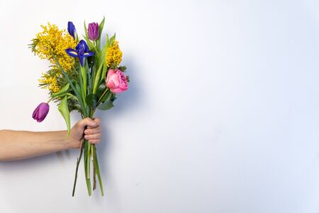 Bouquet of beautiful flowers in mans hand on white background. Minimalistic concept. Space for text.の写真素材