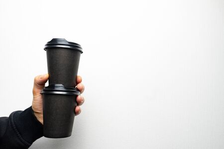Mans hand holds two black paper cups of coffee with black cap. Coffee cup one on another.の写真素材