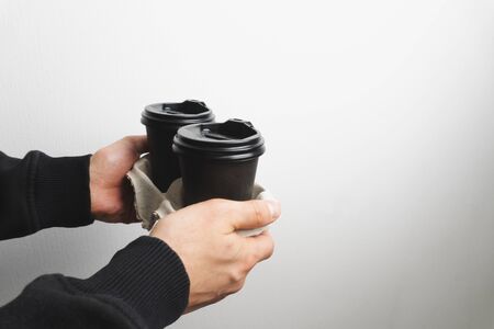 Mans hands hold coffee in coffee black paper cup with clack cap on white background. Close up.の写真素材