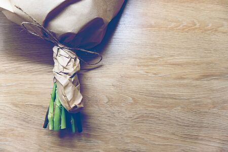 Lower part of flowers bouquet wrapped in crafted paper on wooden background, toned, minimalistic concept, space for text.の写真素材