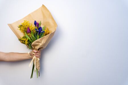 Bouquet of beautiful flowers in mans hand on white background. Minimalistic concept. Space for text.の写真素材