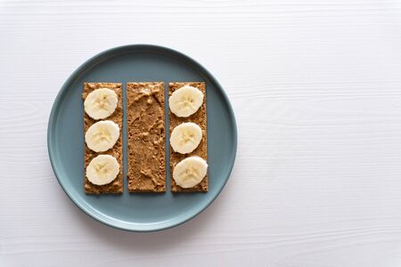 Toasts with peanut butter and banana on round plane on white table, snack for morning breakfast, minimal concept, healthy eatingの写真素材