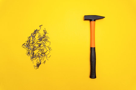 Hammer with orange handle and a pile of stainless nails are on yellow background, minimal housework...