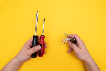 Two different screwdrivers in left male hand and multitool in right mans hand, compare, vs, minimal concept., yellow background. Copy space.の写真素材