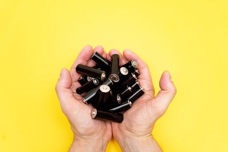 Pile of black aa batteries in mans handful on yellow background, view from the top, minimal concept, copy space.の写真素材