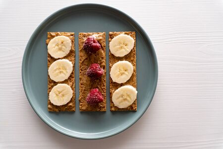Closeup. Raspberry, peanut butter and banana on small bread slices on round plate on white background, toast for morning breakfast or snack for brunch, minimal concept, healthy eating, tonedの写真素材