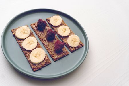 Peanut butter, raspberry and banana on bread slices on round plane on white table, toast for morning breakfast or snack for brunch, minimal concept, healthy eating, tonedの写真素材