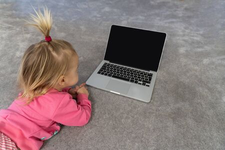 Small cute blond caucasian child laying on floor on grey rug and watching cartoons on laptop. black screen, mockup, copy space,view from top.の写真素材