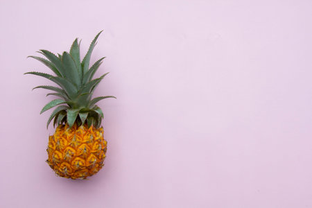 Fresh exotic fruit, yellow pineapple with green leaves on pink background, summer fruit concept,...