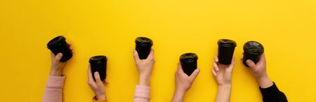 Black takeaway coffee cups with black lids in many caucasian woman and man hands on yellow background, banner, copy space.の写真素材
