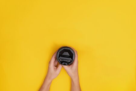 Woman caucasian with take away coffee with black lid on yellow background. Copy space, only hands concept, flatlay, close up.の写真素材