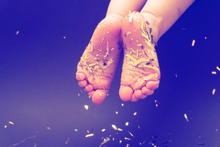 Bare foot caucasian little child legs with gold tinsel at legs and black background, christmas...