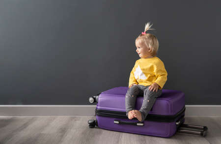 After travel preparation of packing clothes little happy cute blond child sitting on violet luggage, ready for interesting journey after quarantine, lockdown, due to covid. Family travel concept.の写真素材