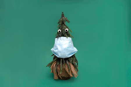 Christmas tree with blue facial medical protective mask and googly eyes on green background, new reality of world desease after lockdown due to covidの写真素材