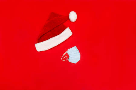 Flatlay with Santa red hat and blue facial protective medical mask on red background, no face, no poeple, Chrisstman conceptual photo, copy space.の写真素材