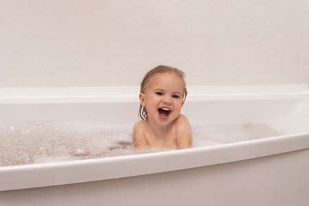 Cute caucasian naked kid plays with white foam at bathroom, laughts, happy childhood concept, white background, copy space.の写真素材
