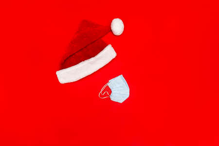 Flatlay with Santa red hat and blue facial protective medical mask on red background, no face, no people, Chrisstman conceptual photo, copy space.の写真素材