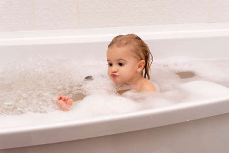Small cute caucasian kid sitting at bath, washing, playing with soap and foam, emotions at little face, indoor, copy space, white background, happy child.の写真素材