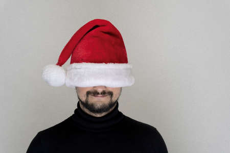 Caucasian bearded man at red Santa cap with hidden eyes copy space, Christmas and new year concept.の写真素材
