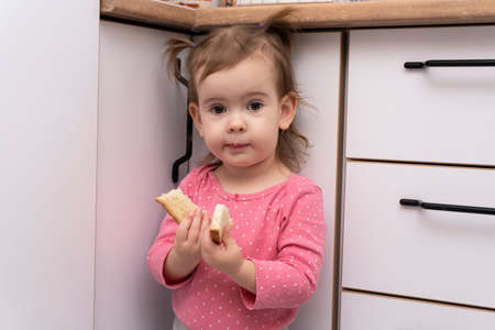 Cute adorable smiling caucasian baby girl eating tasty delicious bread at kitchen, portrait, hungry kid, childhood concept.の写真素材