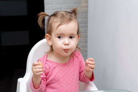 Portrait of cute little pretty caucasian kid eating with funny emotions, smiling, sitting at children chair, white background, copy space, happy healthy children concept.の写真素材
