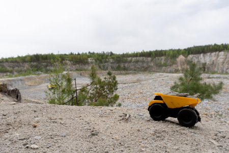 Small yellow car toy, mining truck with stones going up to the hill at the background of quarry. Stones and trees at background and blue sky.の写真素材