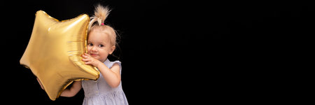 Cute blond caucasian smiling little child holding star balloon at black background, banner format, copy space, holliday celebration conceptの写真素材