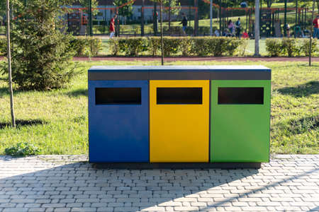 Three colorful recycle bins at urban environment, separately sorting biodegradable trash in different bins summer time, green grass, shadows from recycle bins,waste recycling point outdoor, copy spaceの写真素材