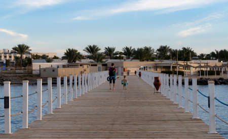 Caucasian man with little kid going at wooden pier and talking, summer time, back view, blue sky with clouds, sea water, outside, happy childhood concept.の写真素材