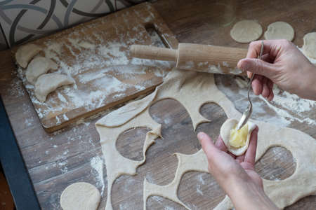 Process of stuffing vareniki, russian traditional dish, woman hands with tea spoon, rolled dough, rollong pin and flout at kitchen table, cooking concept.の写真素材