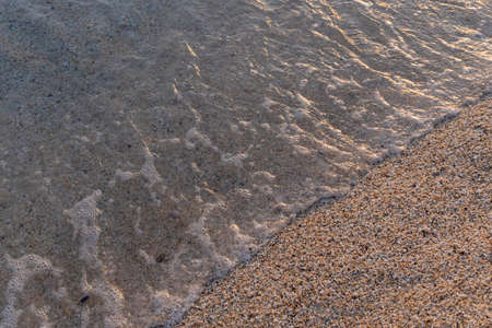 Top view at sandy beach and sea water with waves at sunset.の写真素材
