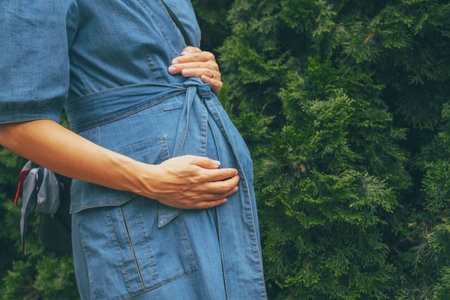 Pregnant caucasian woman in jeans walking at a green park