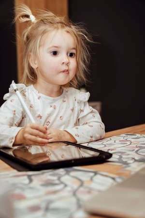 Cute little toddler caucasian girl watching learning lessons on laptop and using ipad for learning, drawing pictures.の写真素材