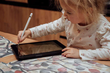 Cute toddler, little blond caucasian child drawing at gadget tablet pad at home, kids using technology.の写真素材