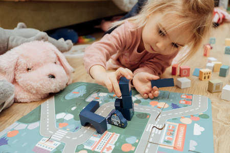 Little caucasian kid playing with wooden toys laying on floor at home.の写真素材