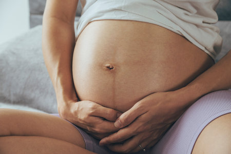 Young pregnant woman sitting on a sofa and holding her belly.の写真素材