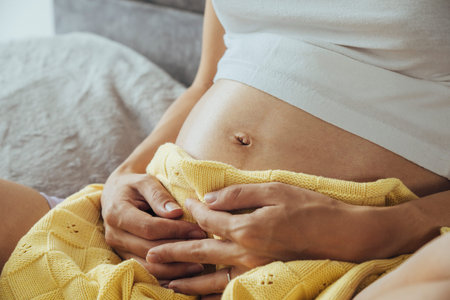 Close up at tummy of young caucasian pregnant woman woth yellow blanket.
