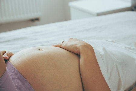 Pregnant caucasian woman laying on a sofa with her arm at tummy, view from a side.の写真素材