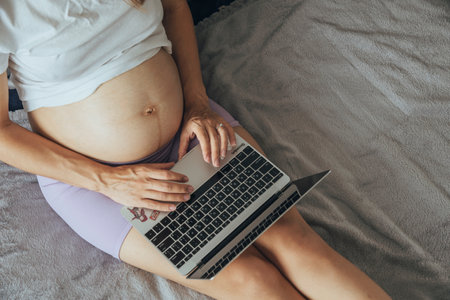 Pregnant caucasian woman working at laptop at home remotely, people using laptop for working at home, view from the top.の写真素材