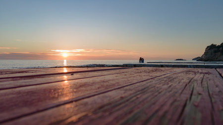 Top of wood table with seascape, sea waves, rocks and people at background, sunset. Empty ready for your product display montage. Summer time vacation background concept, outdoor.の写真素材