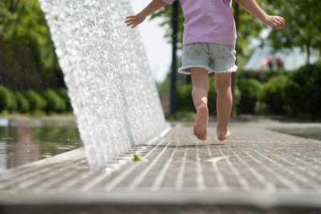 Little caucasian child running near fountain, barefoot. Only legs, no face, view from the back. Summer time. Shot in motion.の写真素材