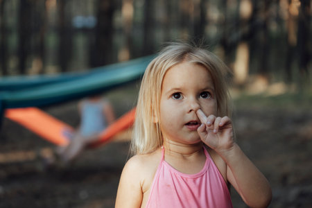 Little caucasian dirty funny child with finger in a nose, emotional face, bad manners, looking up. The kid in a swimming suit. Summer time at nature in a forest, outside.の写真素材