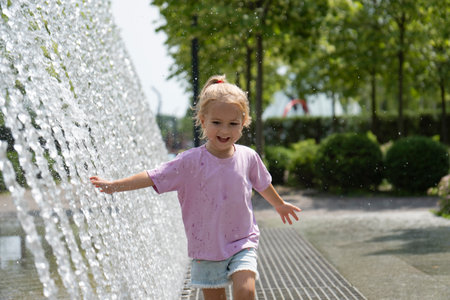 Little caucasian kid running near fountain at part. Happy smiling face. Summer time. Shot in motion. Cute small girl.の写真素材