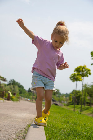 Little cute girl walking on a path, trying to balance. Summer time, green grass at background. Happy childhood, vertical image.の写真素材