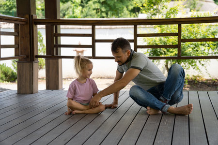 Father learning his daughter to meditate at nature, sitting on wooden floor. Outdoor family activity, peace and health.の写真素材