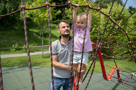 Father helping his daughter climbing at kids playground, summer time together, outdoor family activity.の写真素材