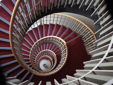 looking directly down a spiral staircase from above with maroon carpet and a wooden handrail