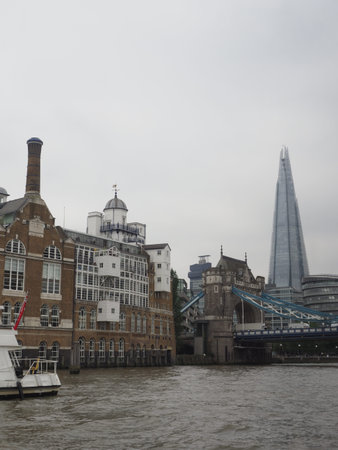 The Shard seen from the river Thames with Tower Bridge in the foreground and some riverside...