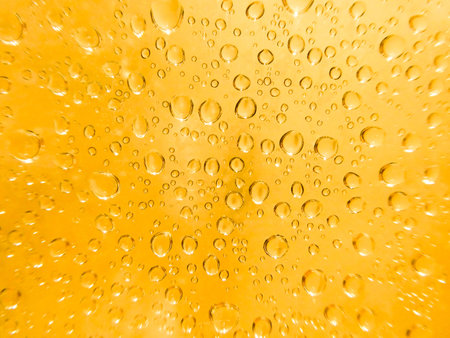 Water drops on glass against a warm yellow background