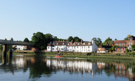 Tranquil evening scene on the River Thames with a red canoe passing a whitewashed pub